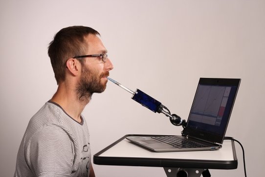 Bild zeigt eine Person, die einen Laptop Computer über die Flipmouse mit dem Mund steuert.