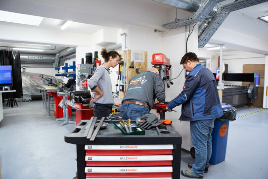 3 Menschen arbeiten in der Metallwerkstatt an den höhenverstellbaren Tisch fürs HappyLab
