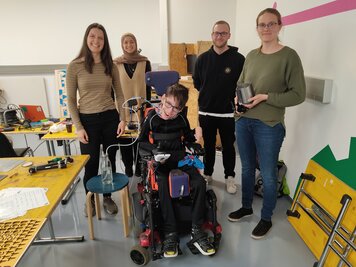 Jannis sitzt im Rollstuhl, dahinter stehen 4 Leute, die beim Trinkverstärker - Projekt geholfen haben.